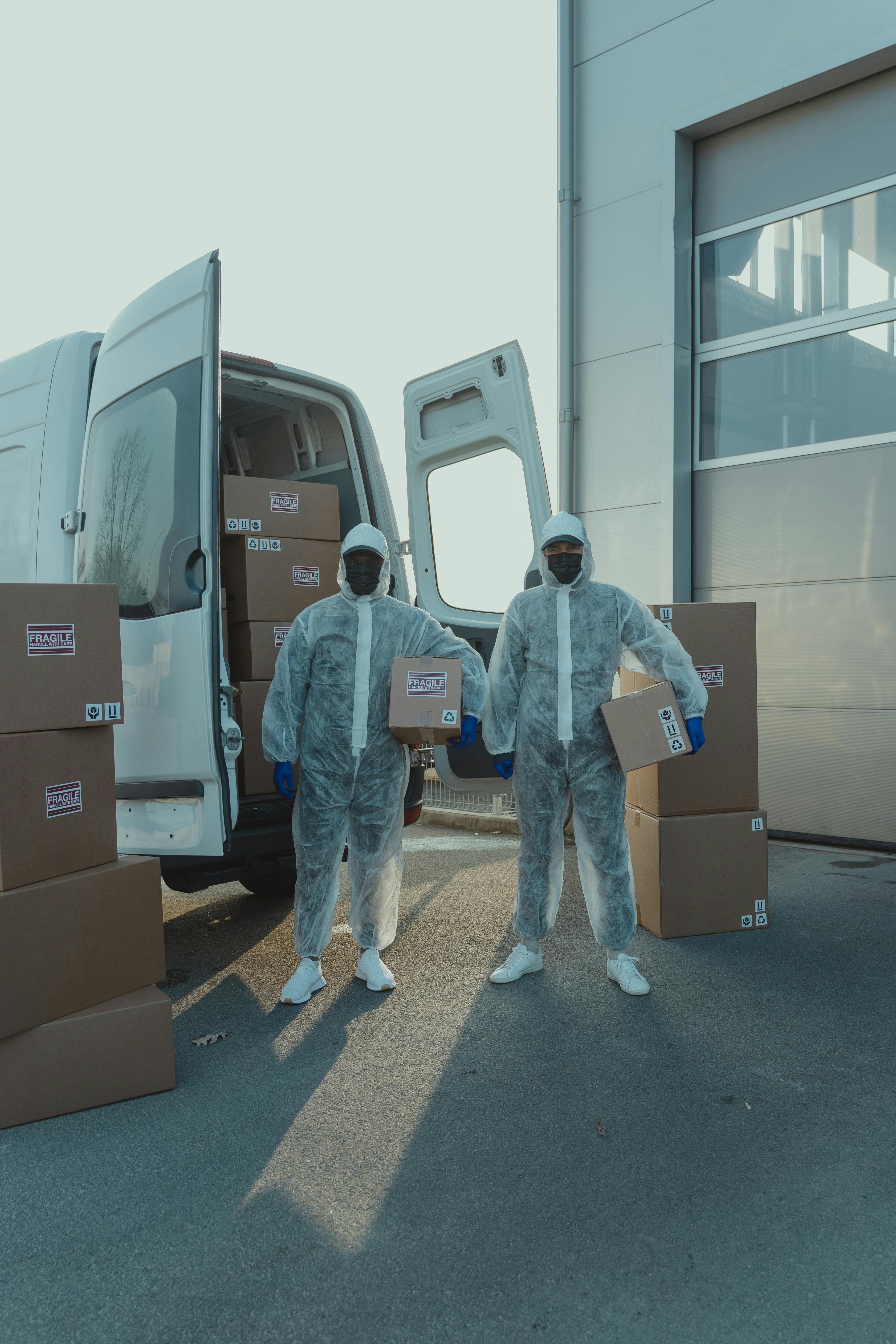 Protected delivery team carrying parcel boxes beside a logistics van